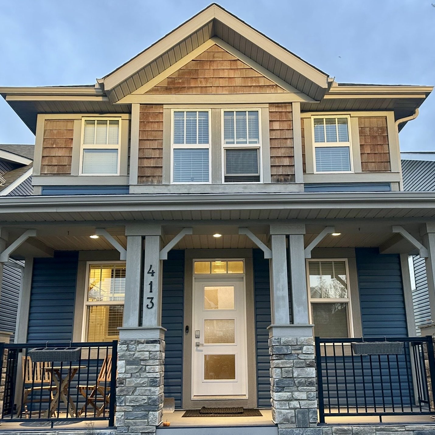 Craftsman two-storey finished in deep blue lap siding with cedar-shake gables, cream trim and a stone-based porch.