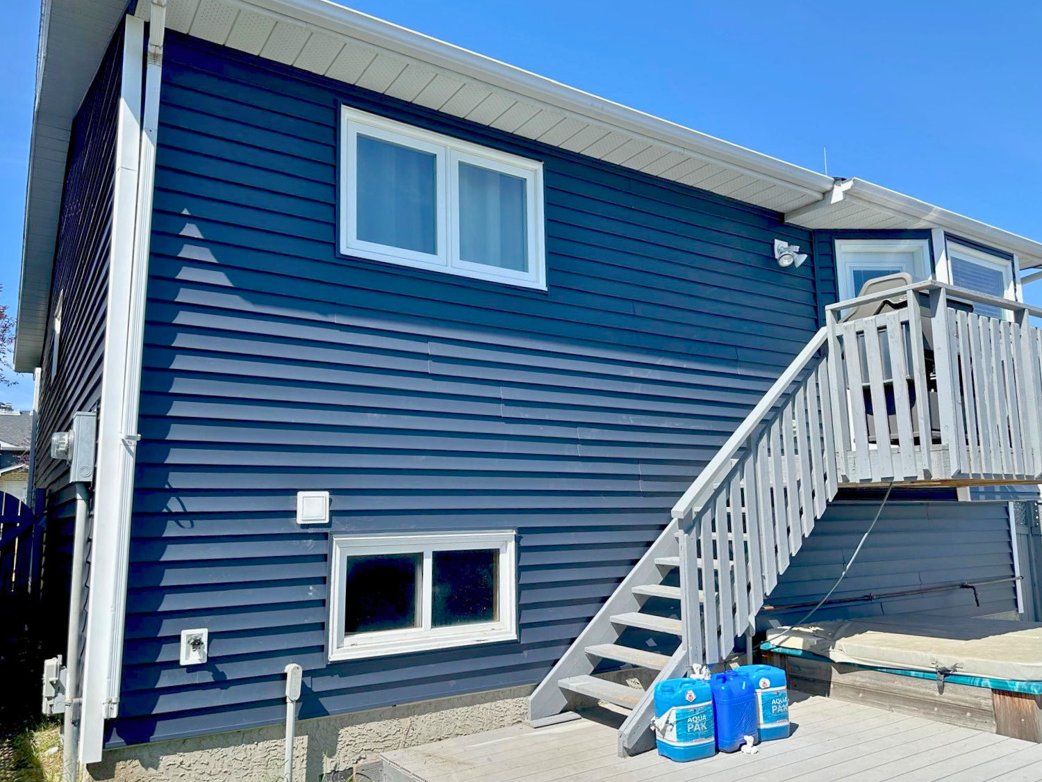 Navy vinyl siding on a garage-suite side wall with new white soffit and exterior stair